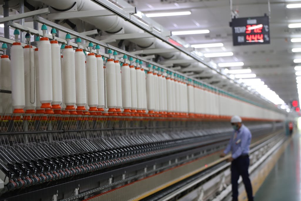A worker manages textile machinery in a modern industrial plant in India.